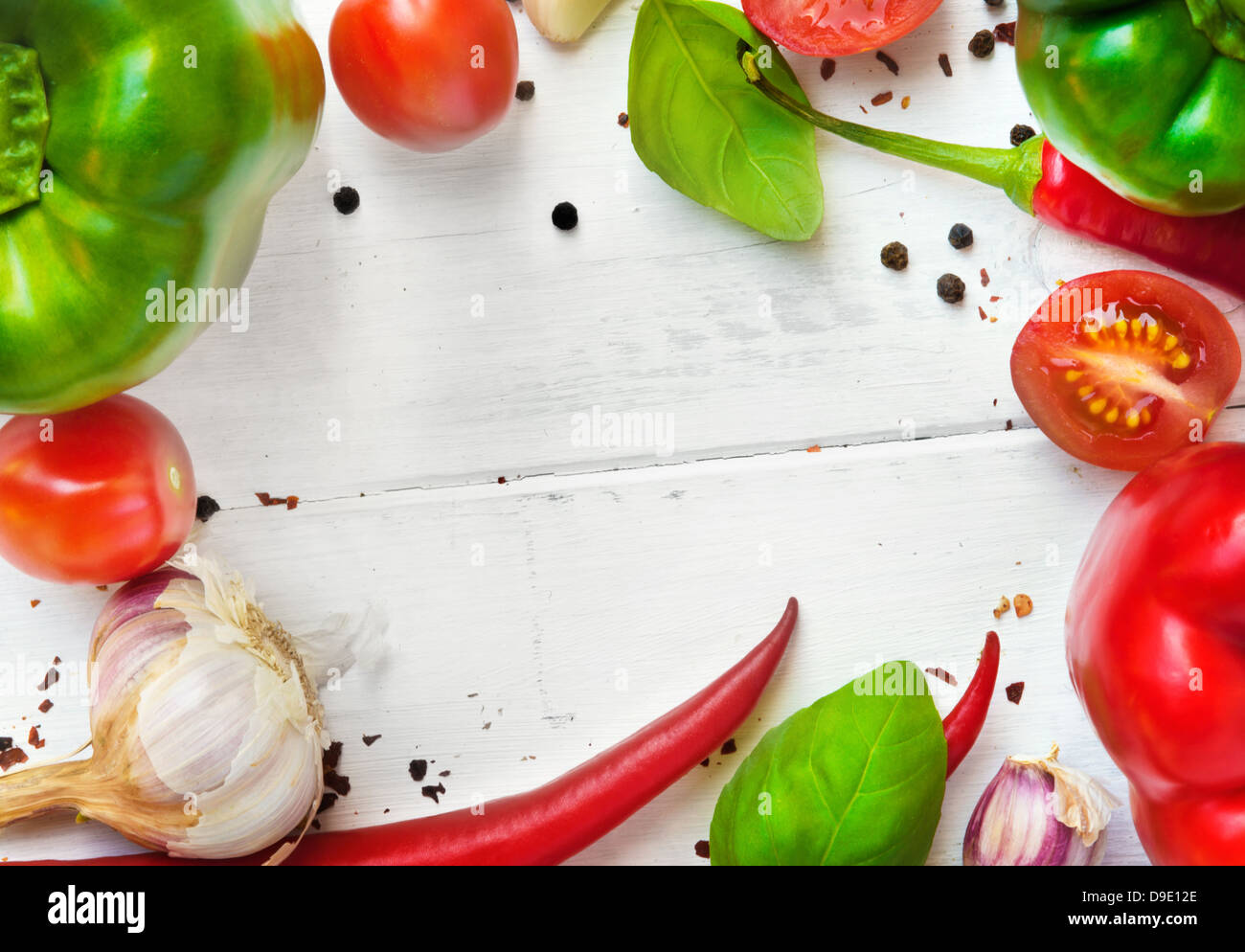 Vegetable frame on the white wooden board ( Red and green bell peppers, chili peppers, garlic, tomatoes, basil leaves, pepper) Stock Photo