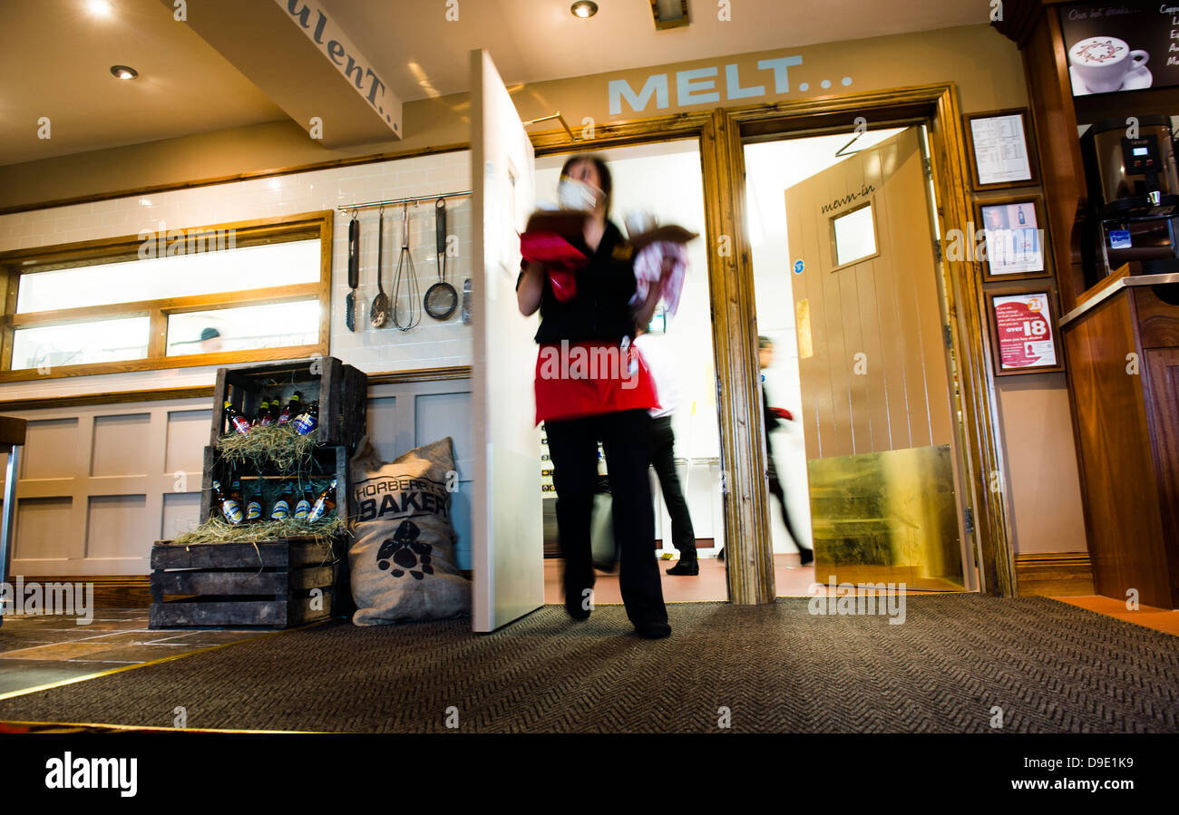As action image waitress emerging from the kitchen of a restaurant carrying plates of food, UK Stock Photo