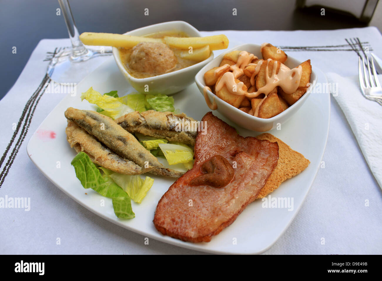 Hot tapas consisting of fried sardines, bacon on a tostada, fries with ...