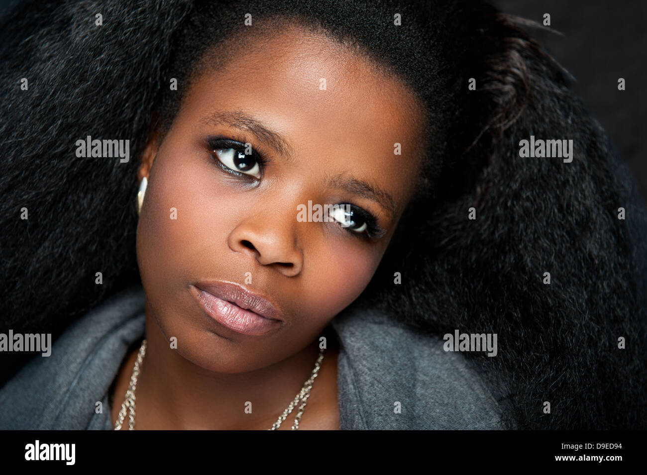 Young African lady with beautiful afro hair and gray coat, a low key background studio shot. Dramatic facial expression. Stock Photo