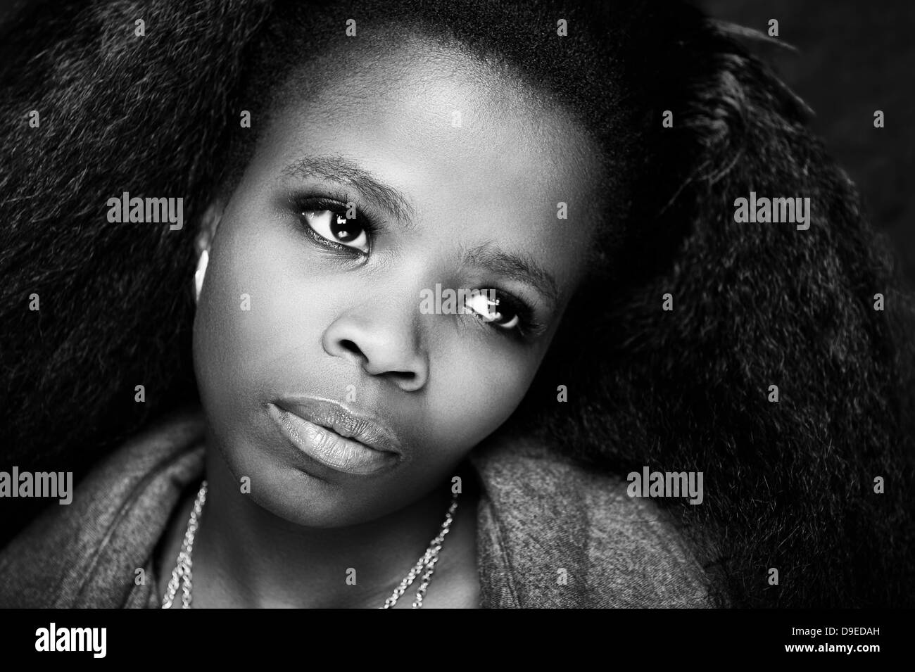 Young African lady with beautiful afro hair, a low key background, black & white studio shot. Dramatic facial expression. Stock Photo