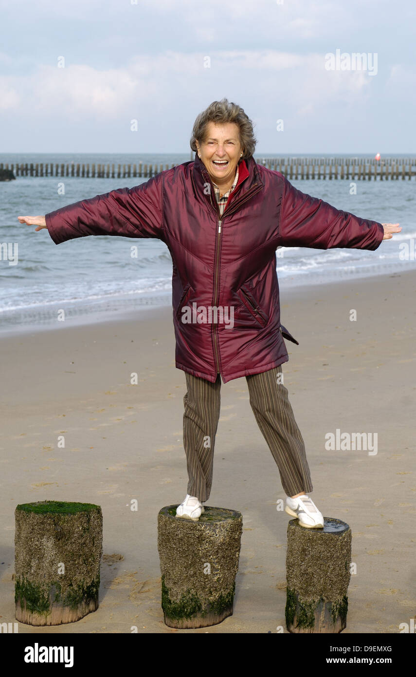 Senior with the beach walk in autumn. Stands in the way with stretched out arms on breakwaters and braces itself to the wind. (M Stock Photo