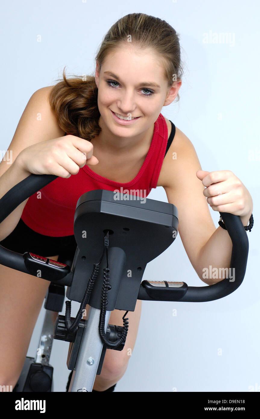 (Model release) Young woman in the red sports shirt sits on a bicycle ergometer Stock Photo