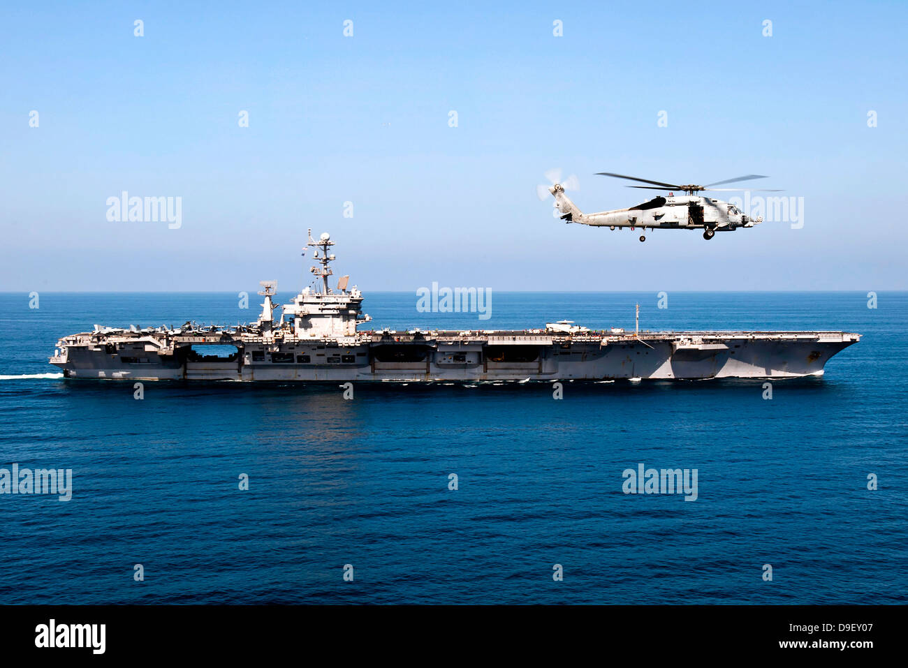 An MH-60R Sea Hawk flies near the Nimitz-class aircraft carrier USS John C. Stennis. Stock Photo