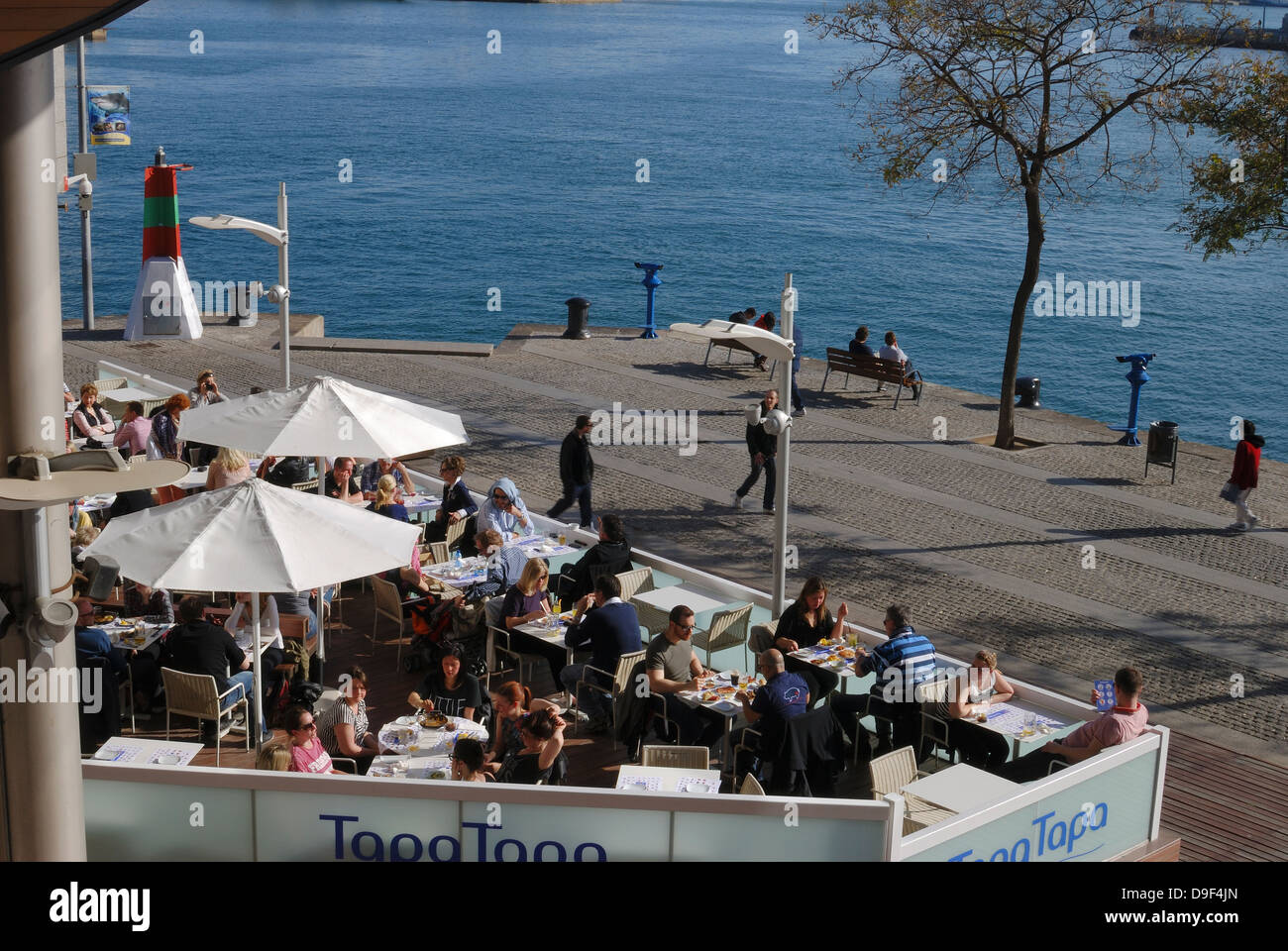 People on outside terrace of restaurant within the modern retail park Port Vell at the harbour in Barcelona. Catalonia. Spain. Stock Photo