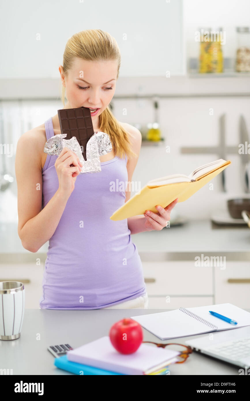 Teenage girl eating chocolate while studying in kitchen Stock Photo
