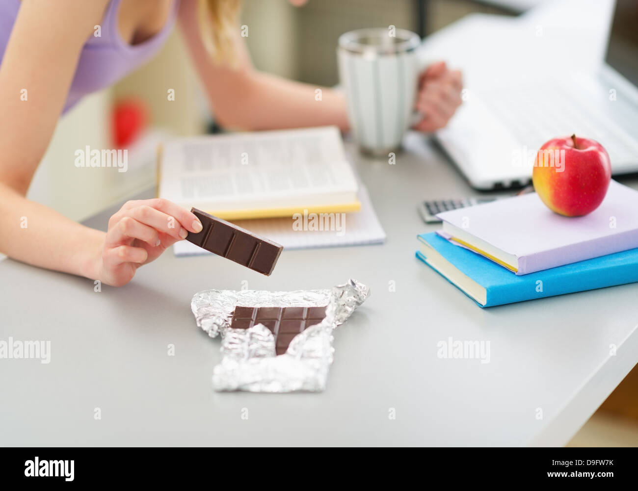 Closeup on teenage girl eating chocolate while studying in kitchen Stock Photo