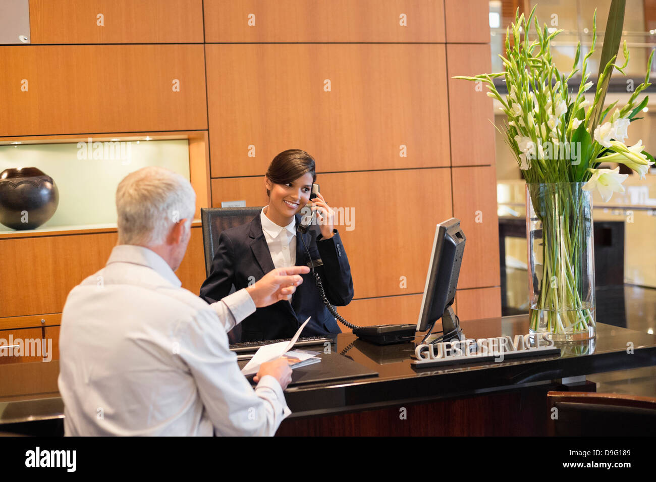 Receptionist talking on a landline phone with a businessman pointing at