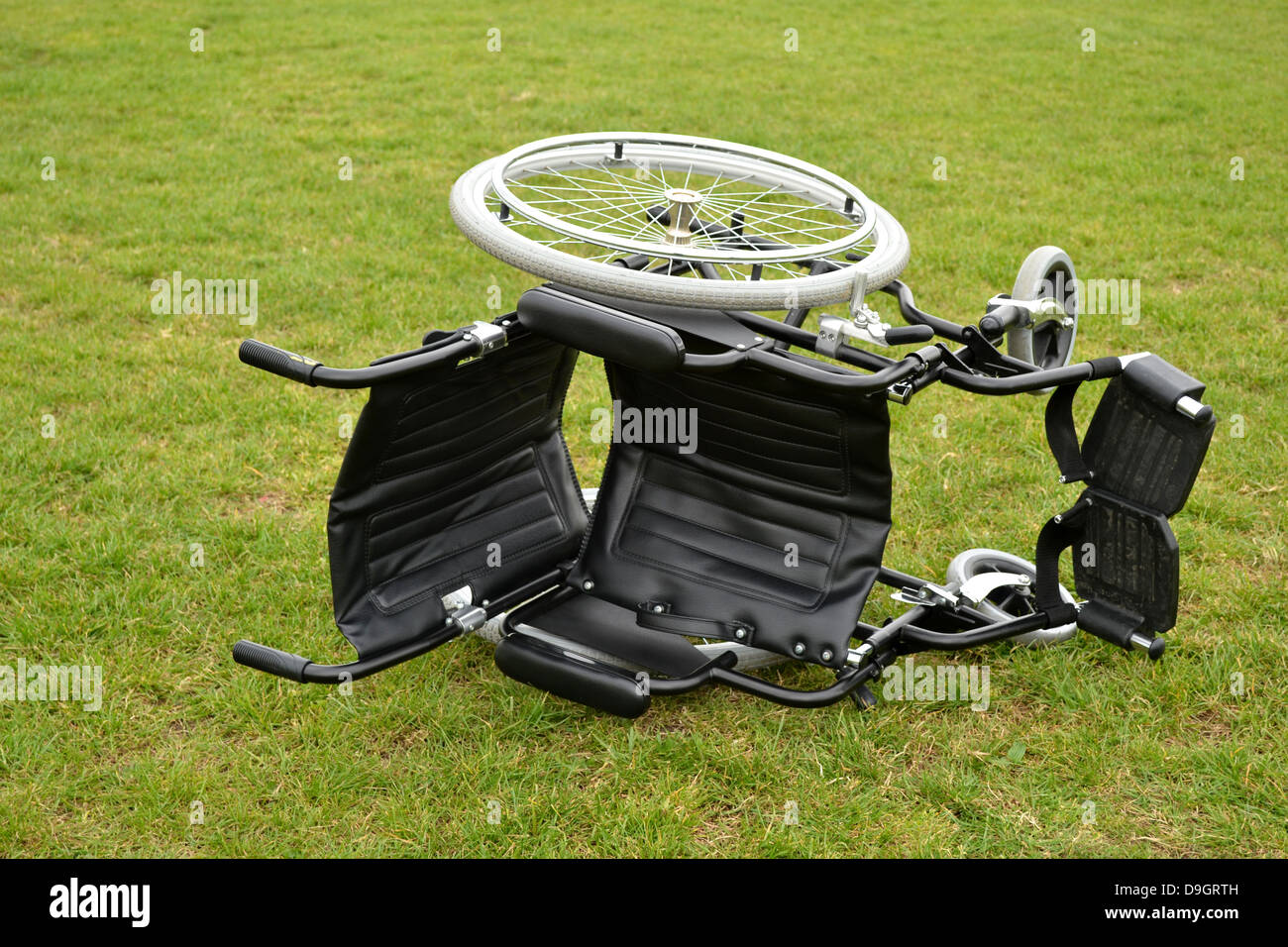 Black wheelchair lying on it's side on a grass lawn Stock Photo Alamy