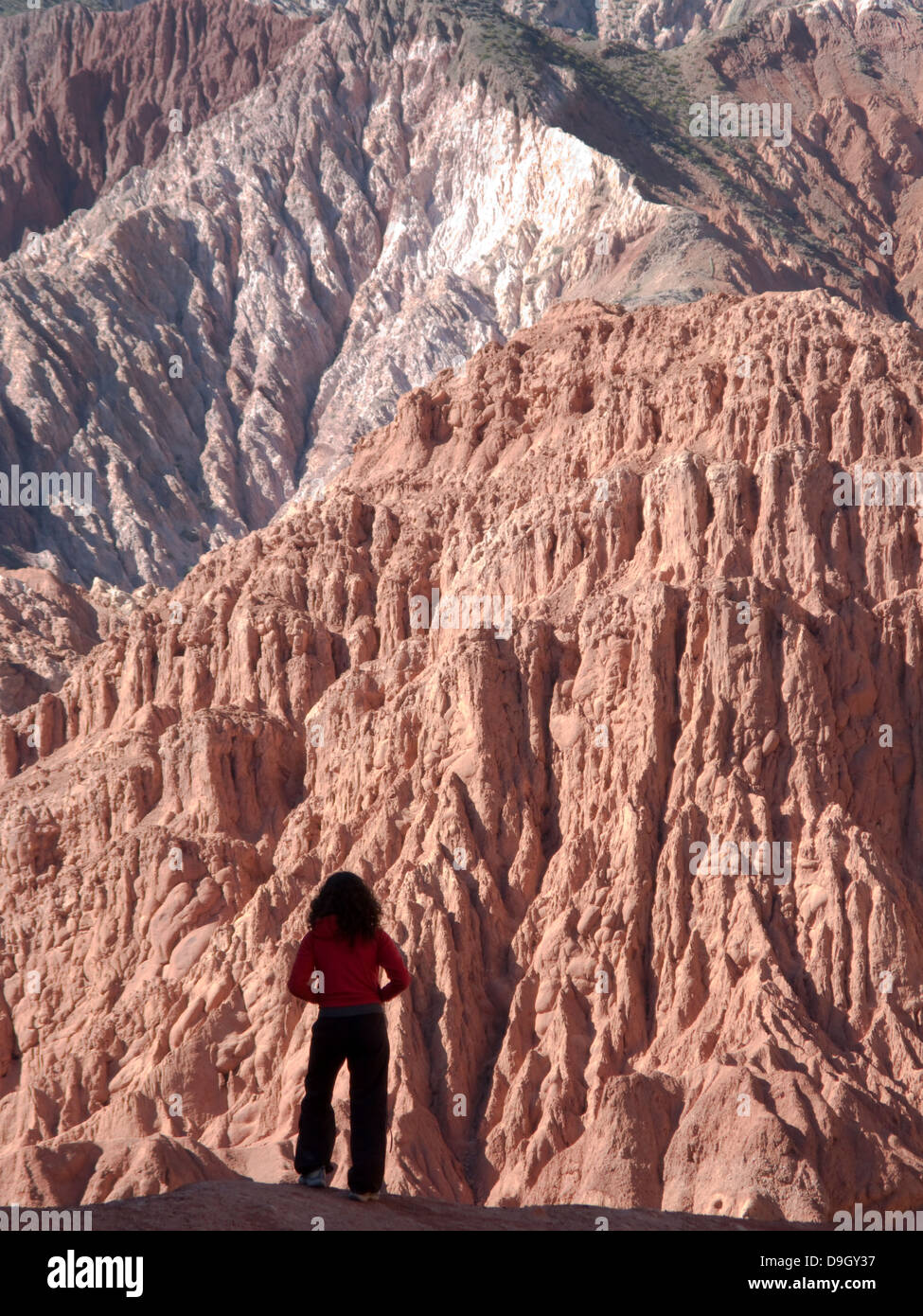 A tourist walks along the Paseo de los Colorados, mountains 'red' surrounding the village of Purmamarca Stock Photo