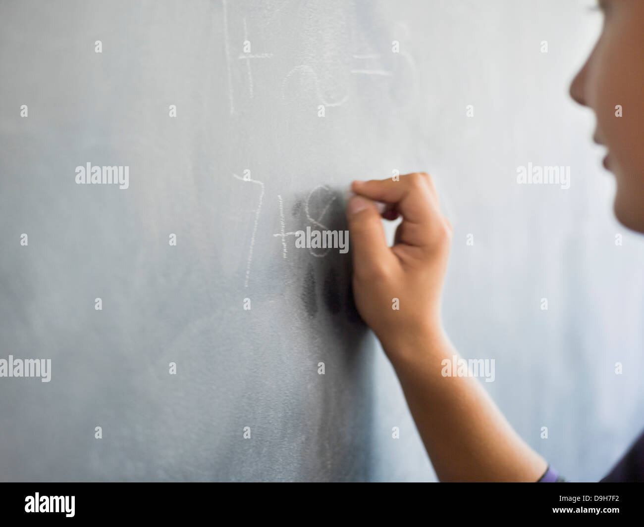 Close-up of a boy writing on a blackboard in a classroom Stock Photo