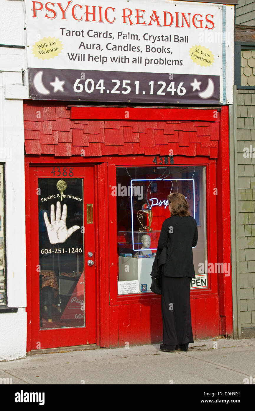 Woman dressed in black looking in the window of a psychic readings and occult shop on Main Street in Vancouver, BC, Canada Stock Photo