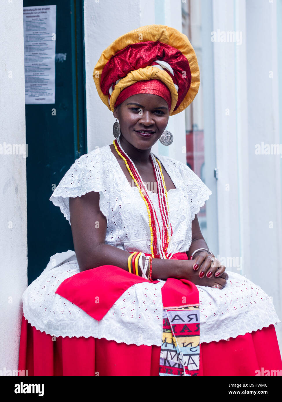 Woman wearing traditional clothes from the Bahia region of Brazil encourages tourists o buy souvenirs in Salvador. Stock Photo
