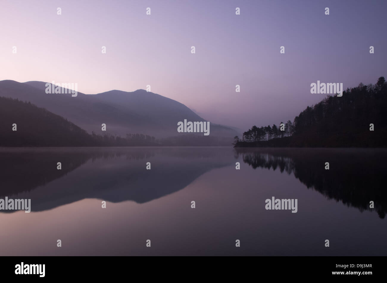 An early morning scene on Thirlmere reservoir with little peninsula covered with tree and mist above the water surface. Stock Photo