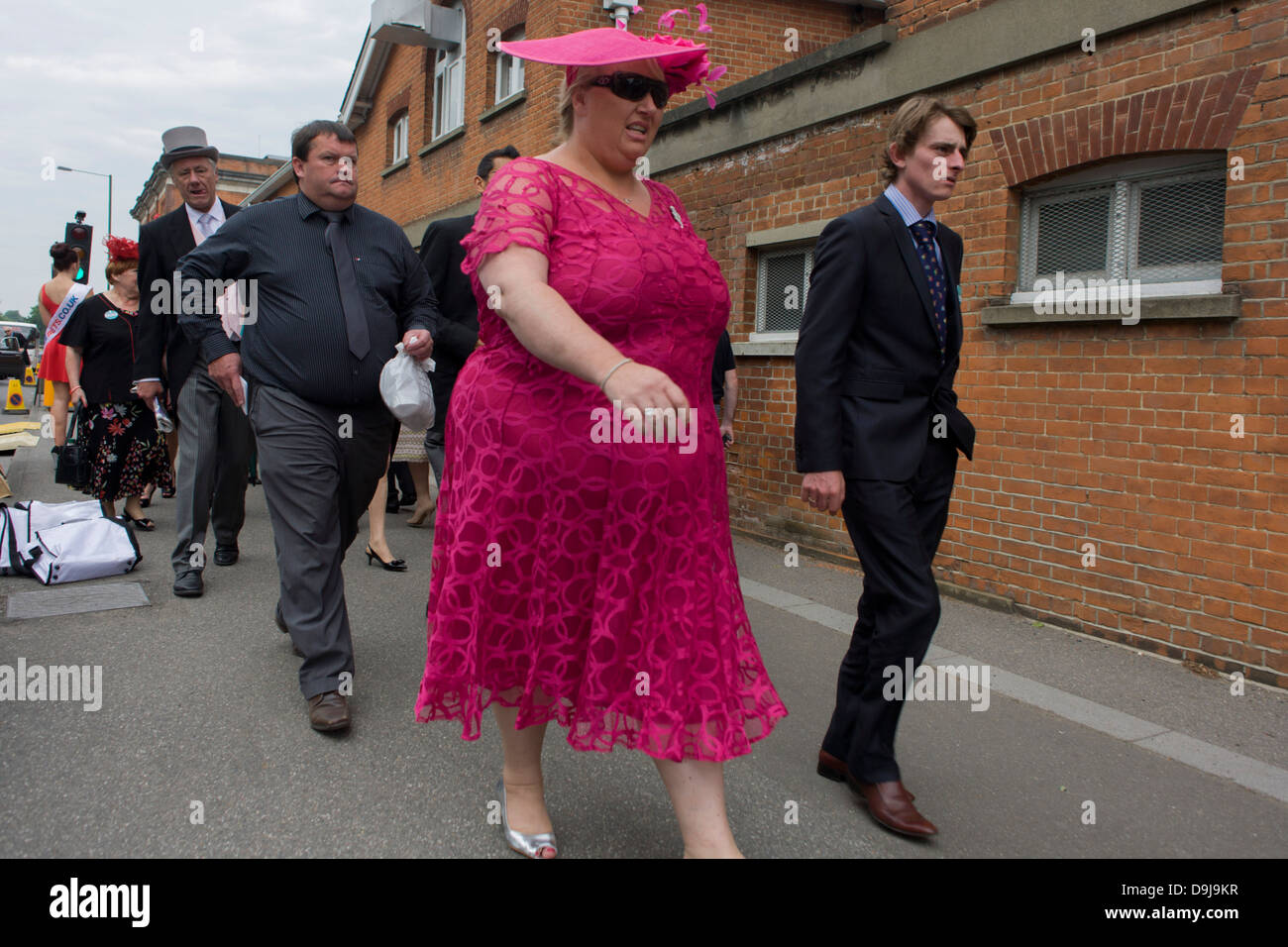 Large lady in pink arrives with family or friends during the annual Royal Ascot horseracing festival in Berkshire, England. Royal Ascot is one of Europe's most famous race meetings, and dates back to 1711. Queen Elizabeth and various members of the British Royal Family attend. Held every June, it's one of the main dates on the English sporting calendar and summer social season. Over 300,000 people make the annual visit to Berkshire during Royal Ascot week, making this Europe’s best-attended race meeting with over £3m prize money to be won. Stock Photo