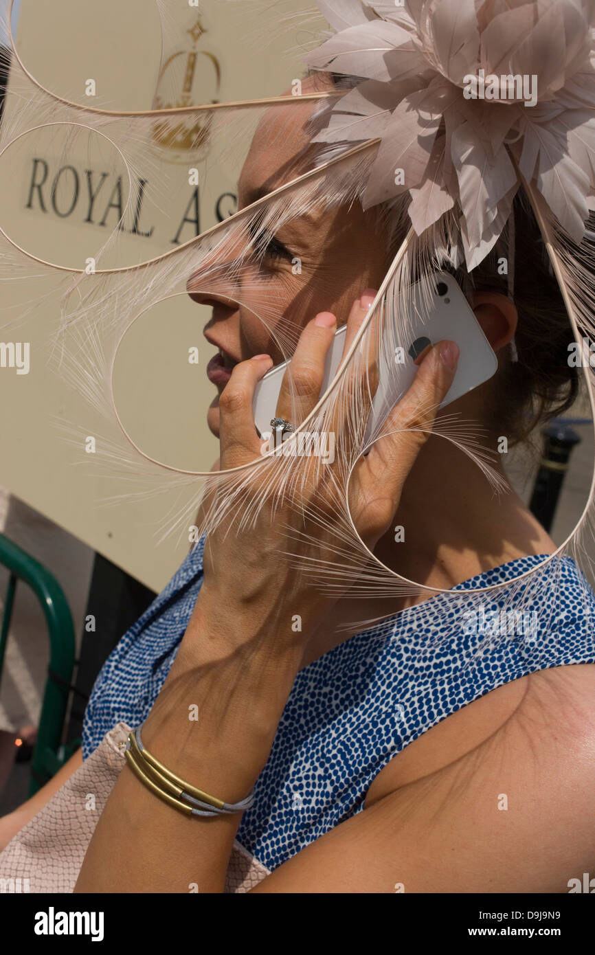 Lady wearing an extraordinary hat makes a call on her smartphone during the annual Royal Ascot horseracing festival in Berkshire, England. Royal Ascot is one of Europe's most famous race meetings, and dates back to 1711. Queen Elizabeth and various members of the British Royal Family attend. Held every June, it's one of the main dates on the English sporting calendar and summer social season. Over 300,000 people make the annual visit to Berkshire during Royal Ascot week, making this Europe’s best-attended race meeting with over £3m prize money to be won. Stock Photo