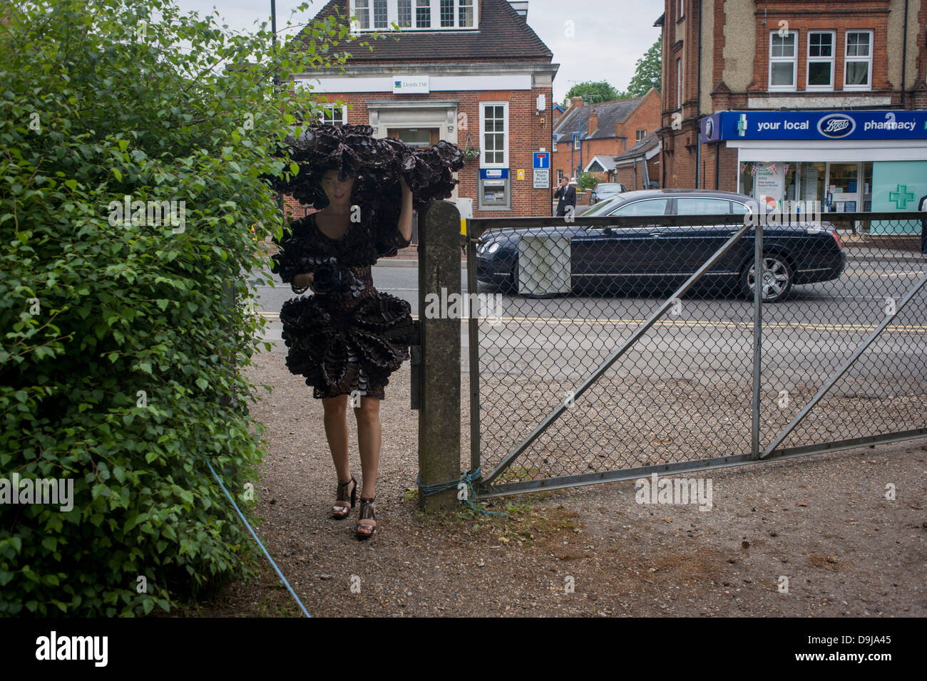 A tall lady wearing an extremely wide hat squeezes through a gap back into a car park after a day's racing during the annual Royal Ascot horseracing festival in Berkshire, England. Royal Ascot is one of Europe's most famous race meetings, and dates back to 1711. Queen Elizabeth and various members of the British Royal Family attend. Held every June, it's one of the main dates on the English sporting calendar and summer social season. Over 300,000 people make the annual visit to Berkshire during Royal Ascot week, making this Europe’s best-attended race meeting with over £3m prize money to be wo Stock Photo