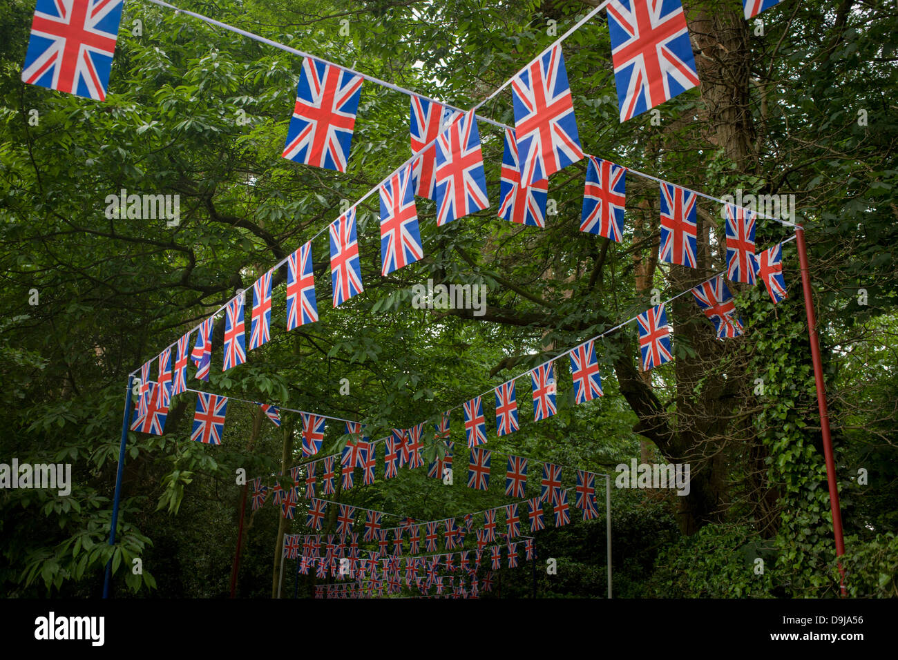 Hundreds of union jack flag bunting stretches back downhill through woods towards the local station during the annual Royal Ascot horseracing festival in Berkshire, England. Royal Ascot is one of Europe's most famous race meetings, and dates back to 1711. Queen Elizabeth and various members of the British Royal Family attend. Held every June, it's one of the main dates on the English sporting calendar and summer social season. Over 300,000 people make the annual visit to Berkshire during Royal Ascot week, making this Europe’s best-attended race meeting with over £3m prize money to be won. Stock Photo