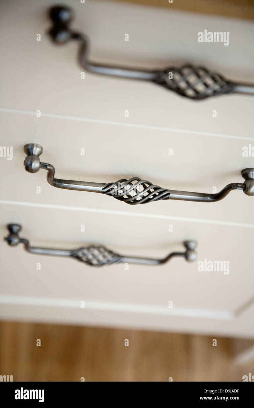 Ornate pewter effect handles on white chest of drawers photographed from above showing woven cut-out detail against wooden floor Stock Photo