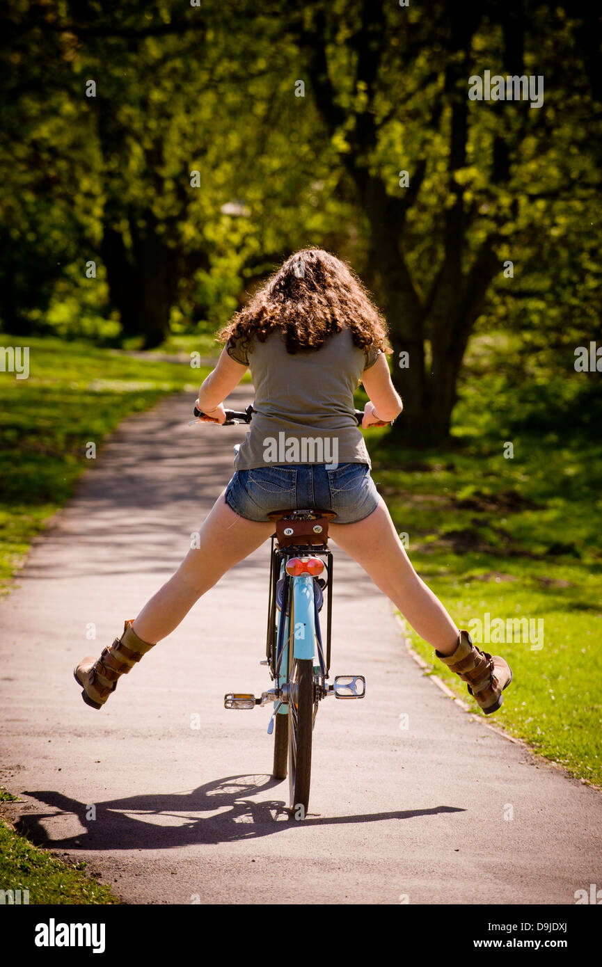 Rear view of a caucasian woman with long curly brown hair free wheeling out of shot on traditional bicycle. Stock Photo