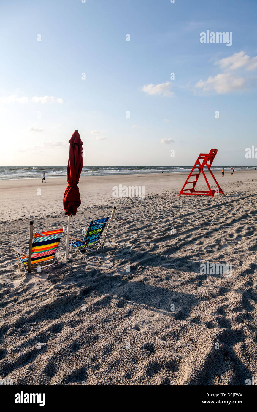 Colorful striped folding beach chairs and folded red umbrella with