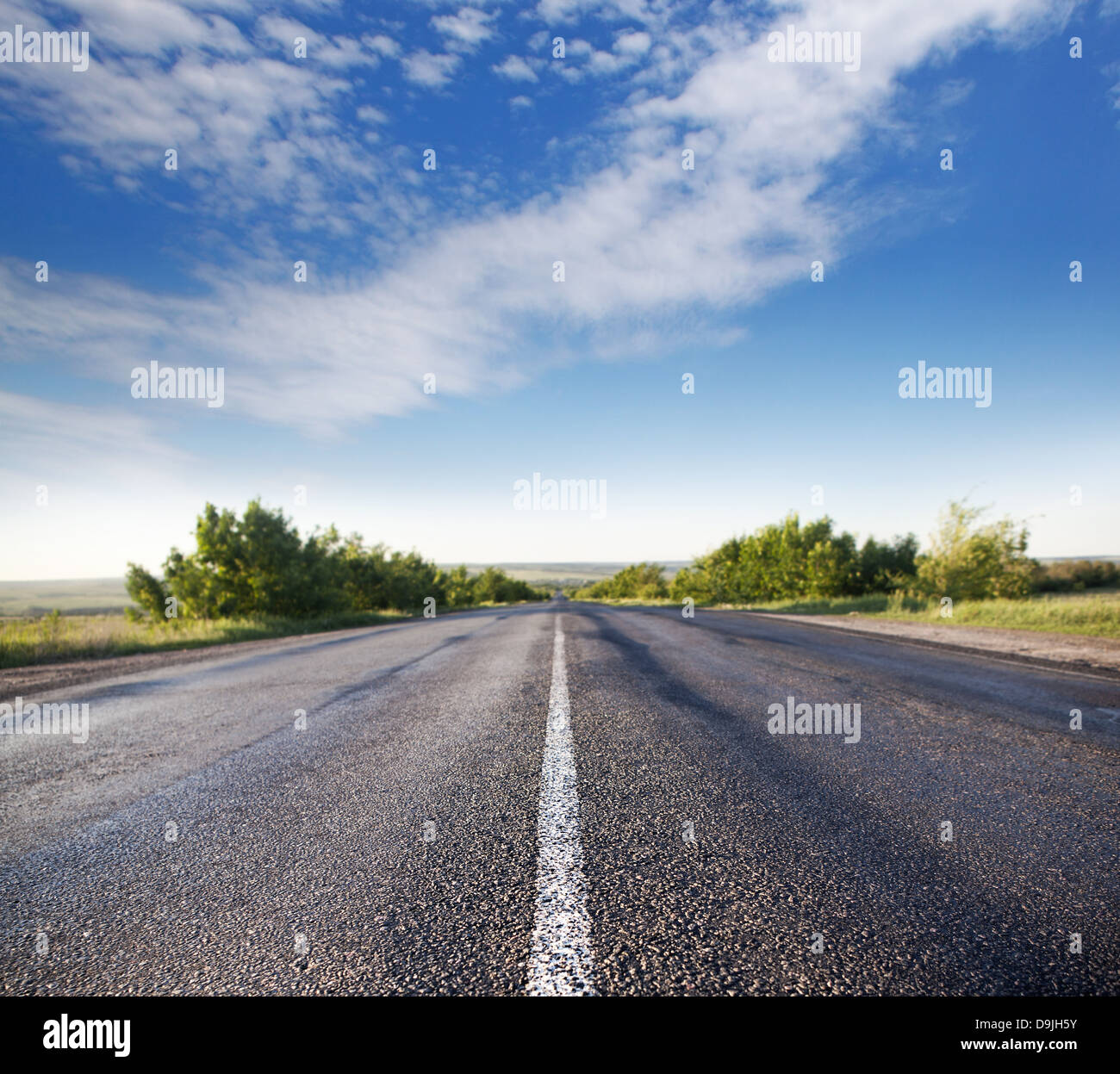 asphalt road through the green field and clouds on blue sky in summer ...