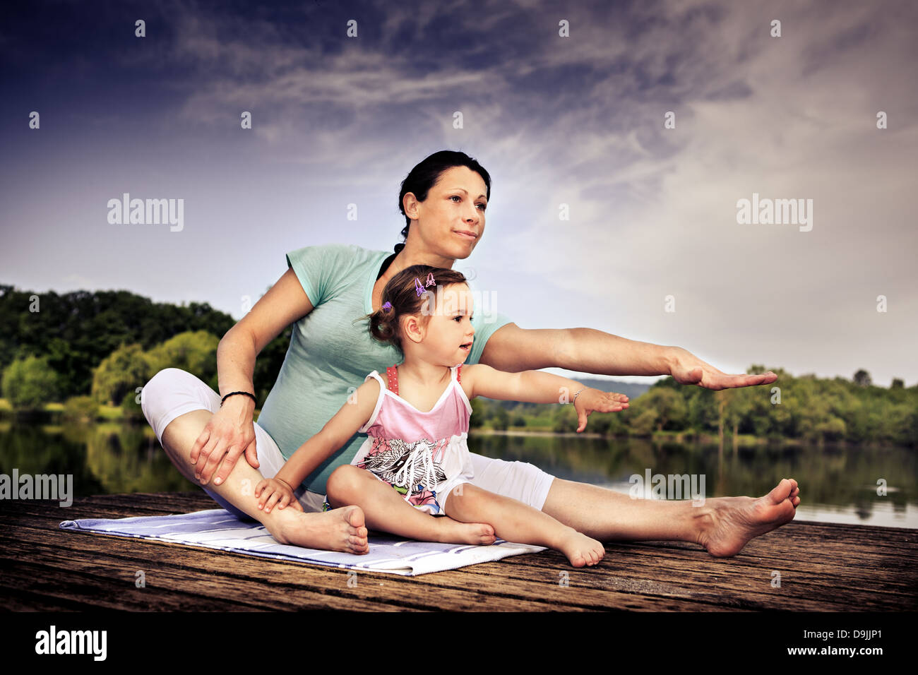pregnant woman and her little daughter making yoga exercise at a lake Stock Photo