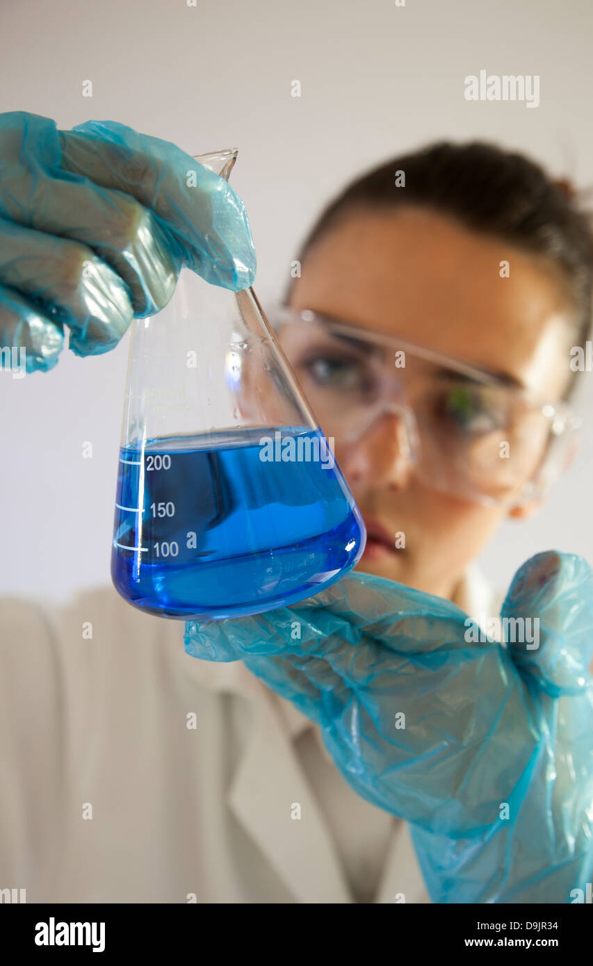 Female lab technician or scientist holding a glass beaker with blue liquid. Stock Photo
