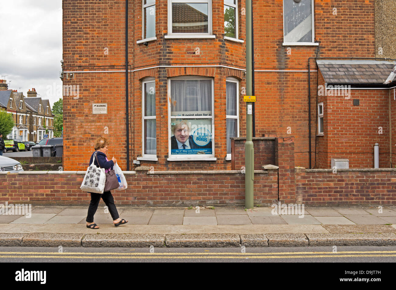 Woman walks past house which has a Boris Johnson Mayoral election campaign poster in the window. Stock Photo