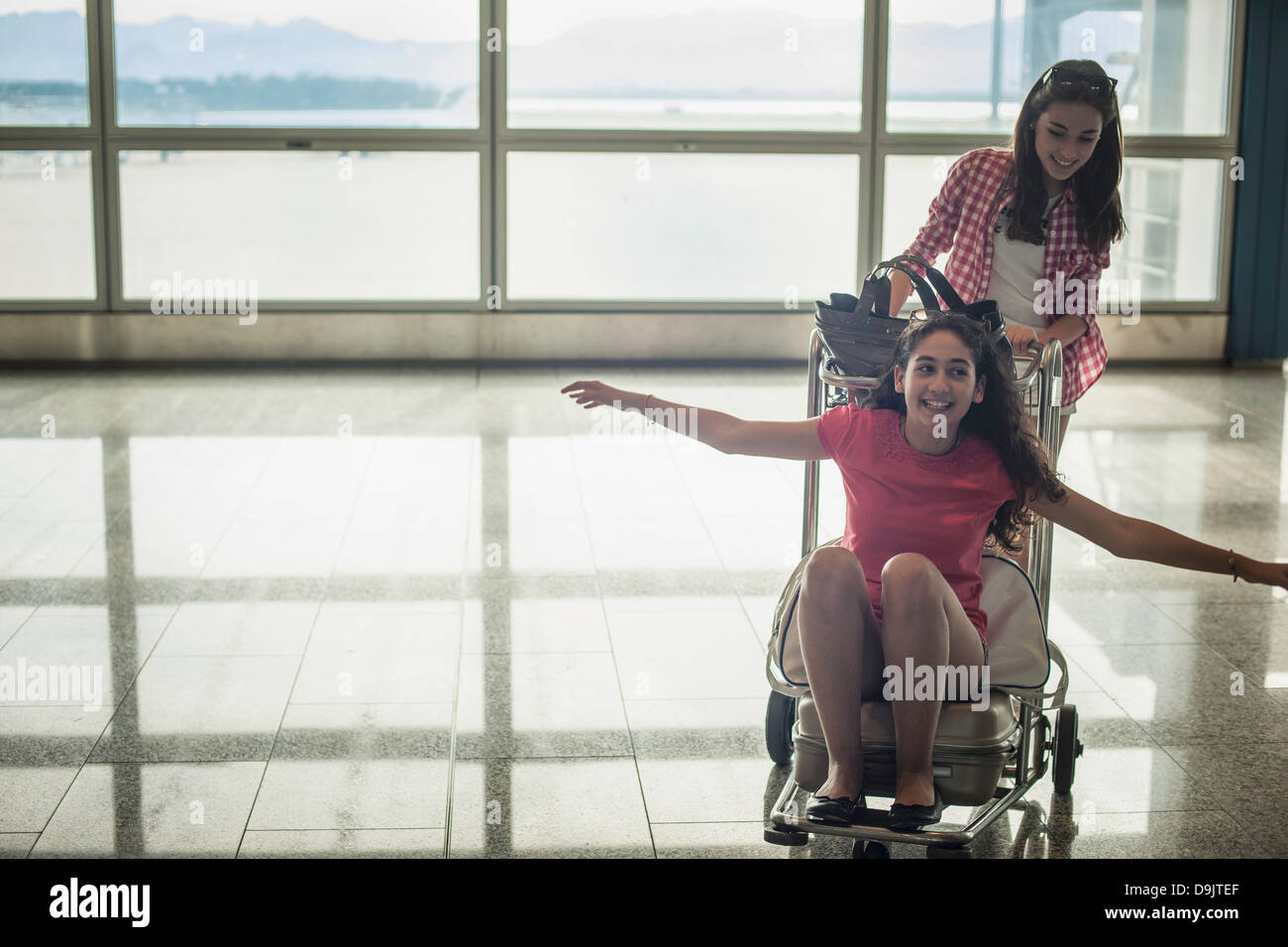 Teenage girl pushing friend on luggage trolley Stock Photo