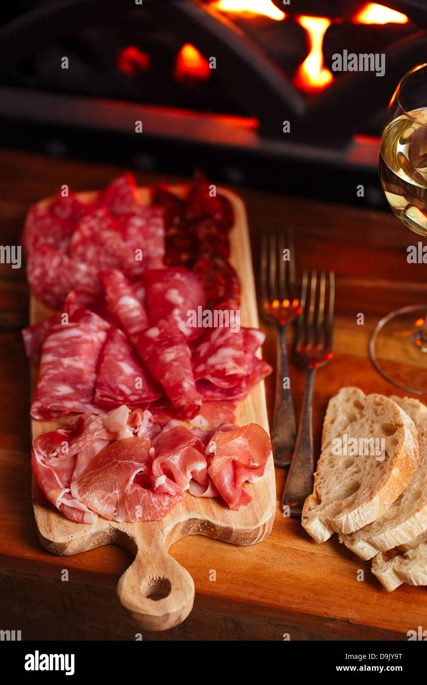 Platter of serrano jamon Cured Meat with cozy fireplace and wine background Stock Photo