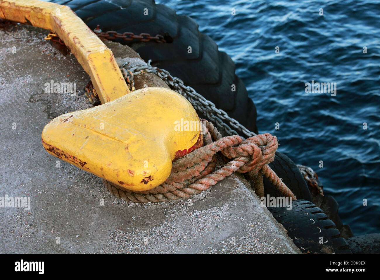 Yellow mooring bollard with blue naval rope and chain on the pier Stock Photo