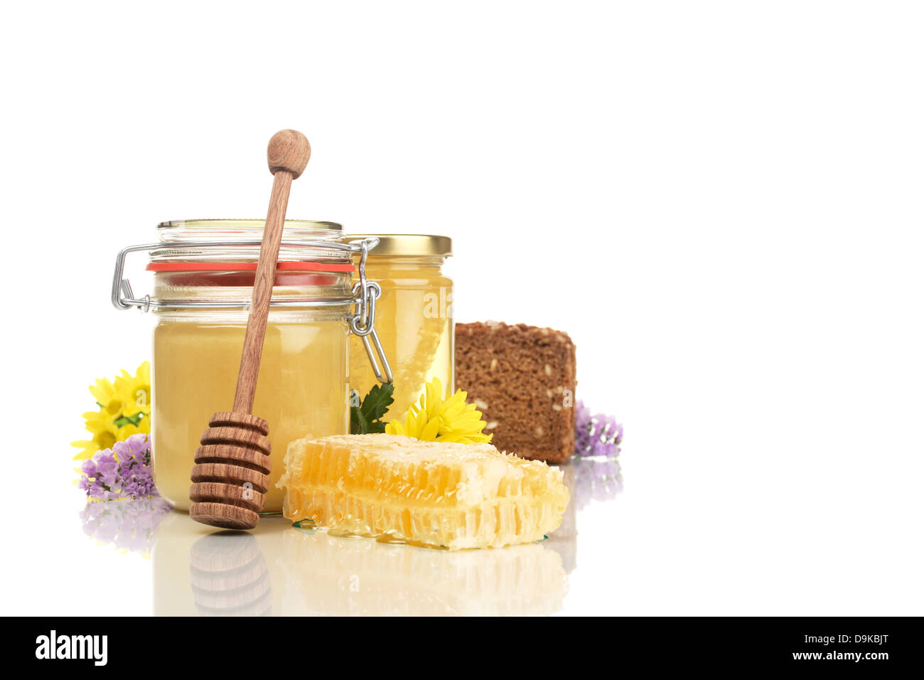 Honey glasses with honeycomb, wholemeal bread, honey spoon and flowers, Honeycomb jars with honey, wholemeal bread, honey and fl Stock Photo