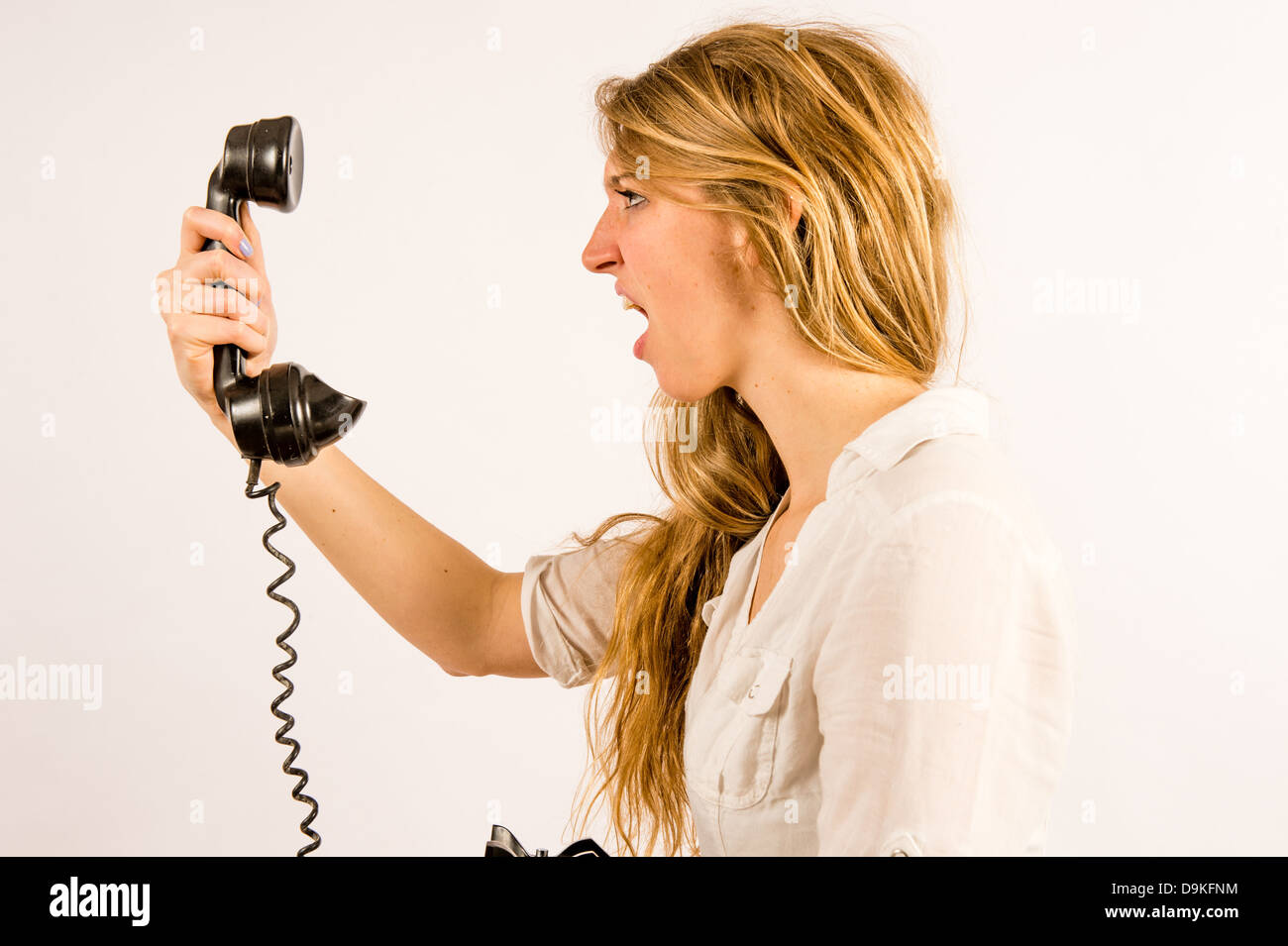 Poor customer helpline service: An angry young woman shouting yelling into an old retro telephone receiver - Stock Photo