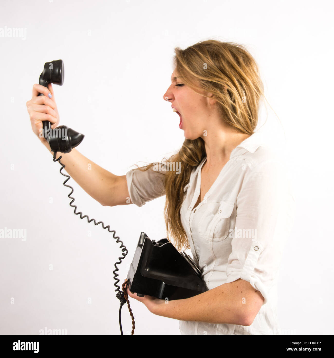 Poor customer helpline service: An angry young woman shouting yelling into an old retro telephone receiver Stock Photo