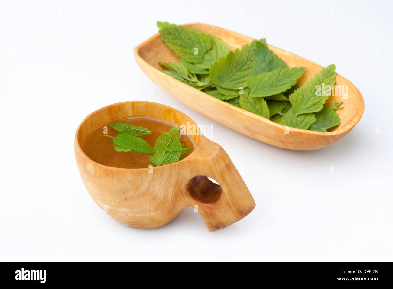 Lemon Balm (Melissa officinalis) Herbal Tea in a Kuksa Alongside a Wooden Bowl Containing the Leaves Stock Photo