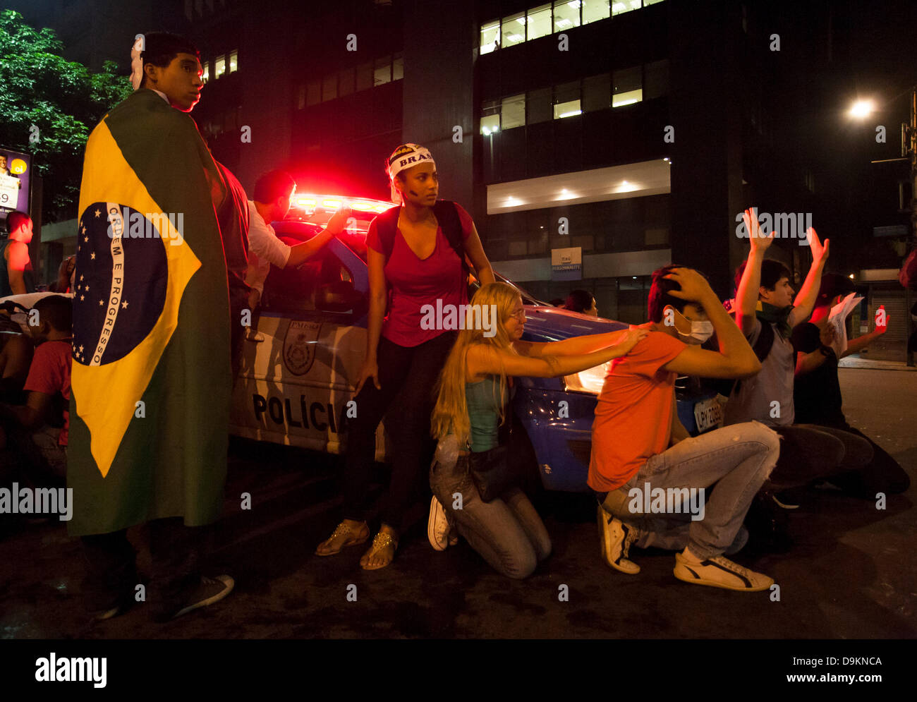 Rio de Janeiro, Brazil  20th June 2013. Frightened protesters shelter around a military police car in Avenida Rio Branco, as the ´Batalhão de Choque´, Riot Control Police´ pass by close by, after dispersing protesters using tear gas and rubber bullets in the centre of Rio de Janeiro, Brazil  20th June 2013 Credit:  Peter M. Wilson/Alamy Live News Stock Photo