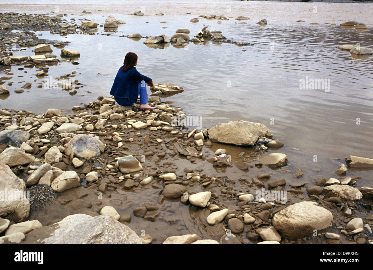 Lone young Chinese woman siting at the shore of the Huang He Yellow river flowing through Lanzhou city Gansu province China Stock Photo