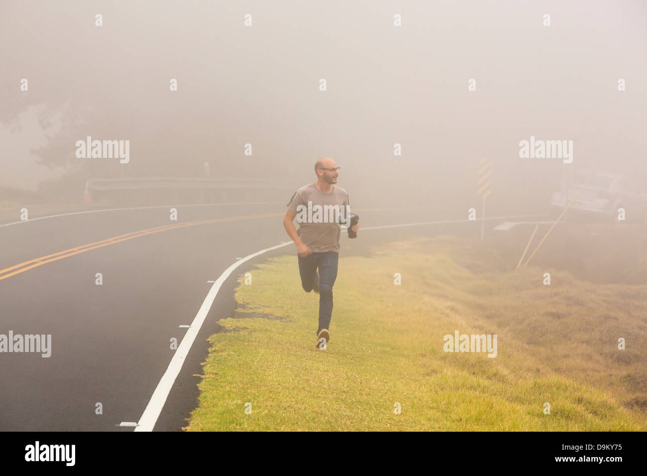 Mid adult man running along roadside with camera Stock Photo