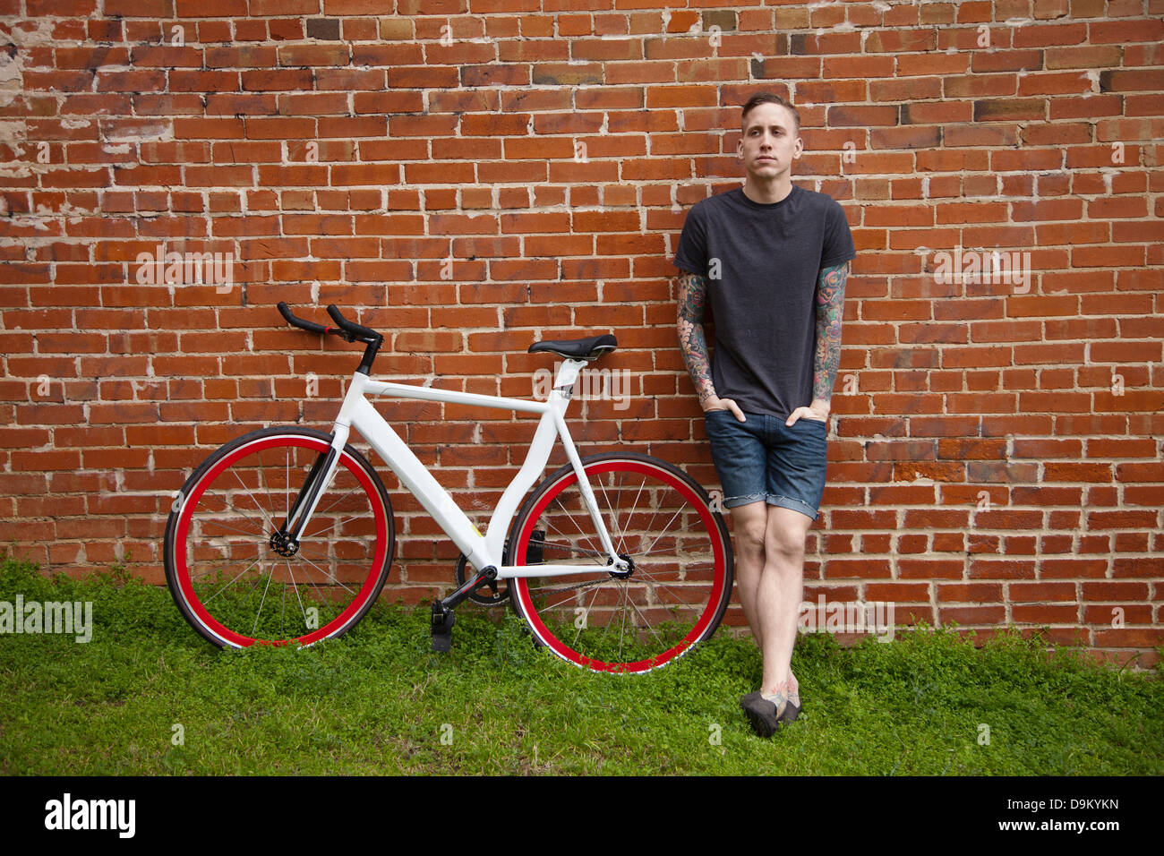 Young tattooed man leaning against brick wall Stock Photo - Alamy