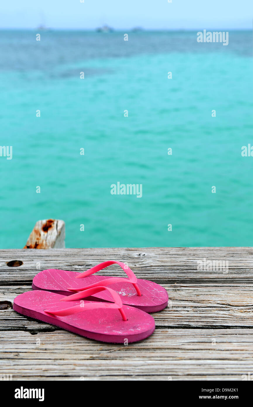Pair of pink flip flops on wooden pier with ocean in background Stock Photo