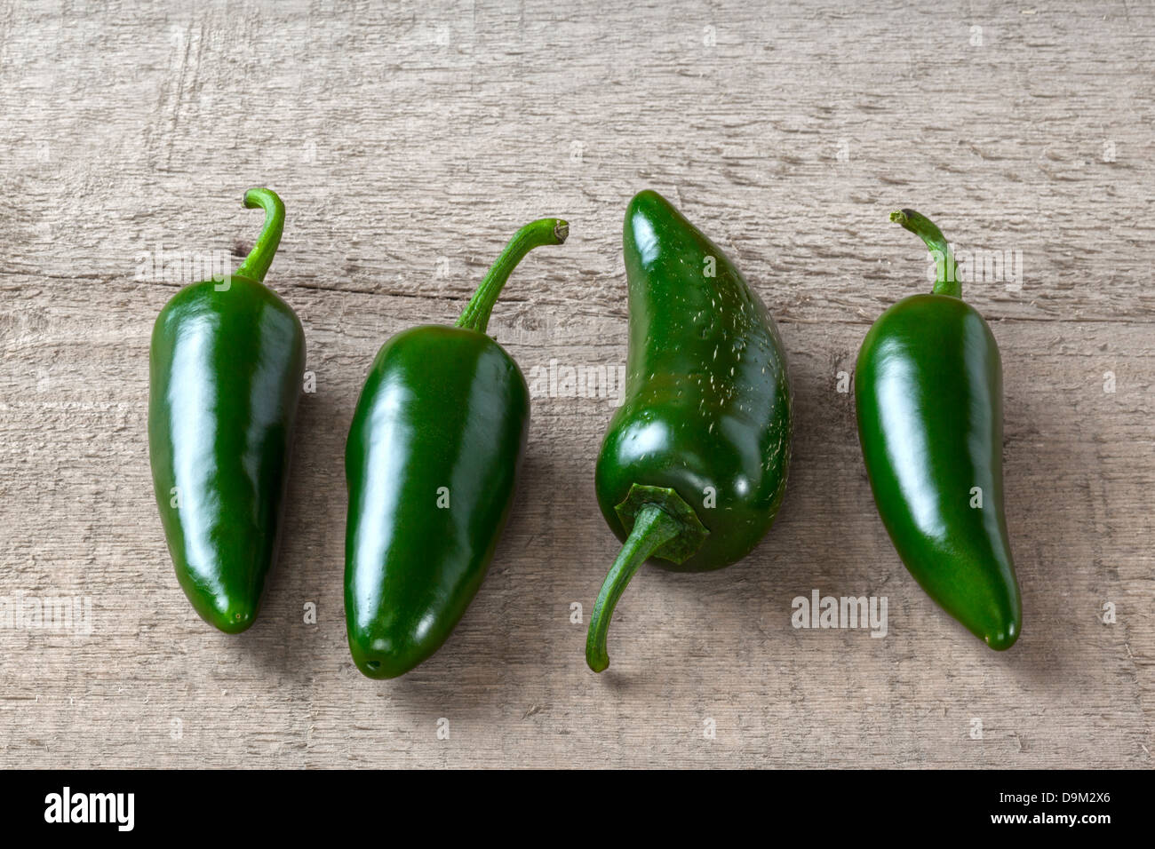 Green Jalapeno Chillies - four jalapeno chillies on a plank or rustic background. Stock Photo