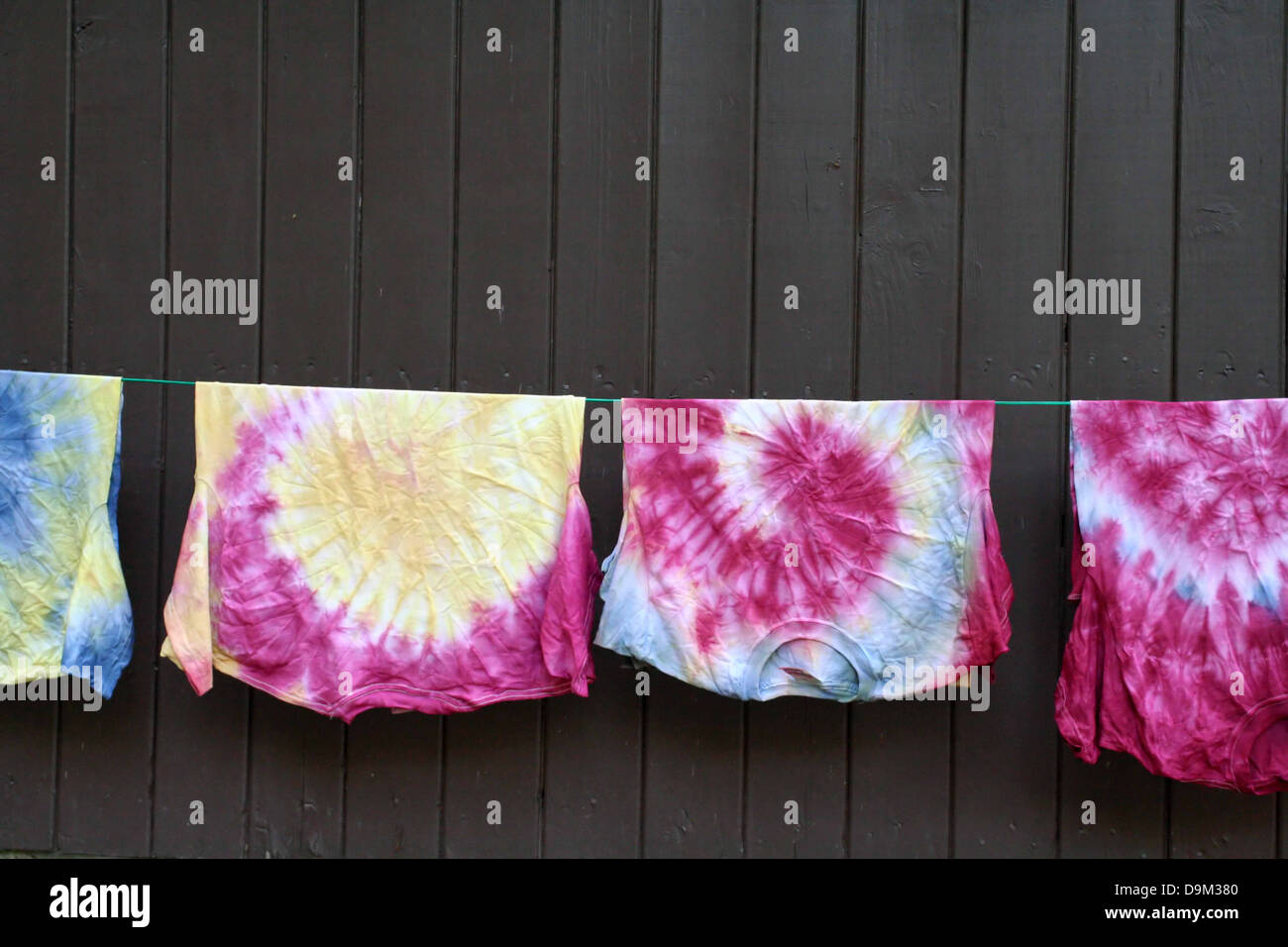 shirts t-shirts tee shirt clothsline rope hanging hang dry colors colored tie dye tie-dye brown wood wall Stock Photo