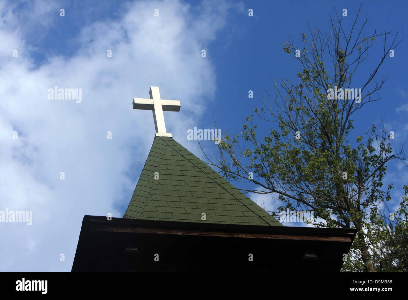 Christian church chapel steeple cross roof clouds blue sky trees Stock Photo