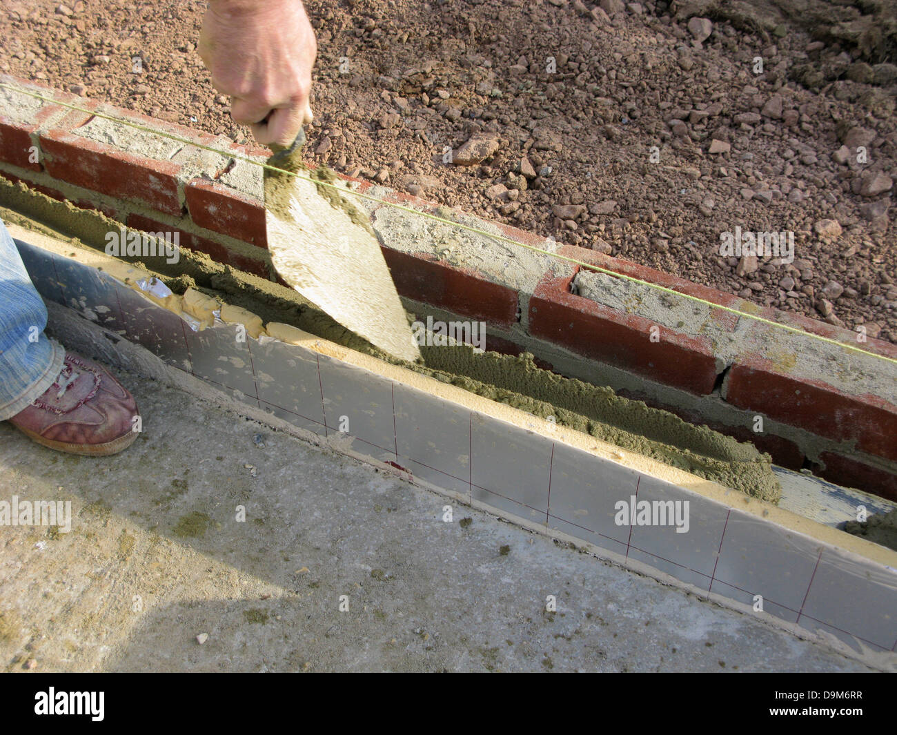 builder / construction placing cementing in the space for thermalite bricks Stock Photo