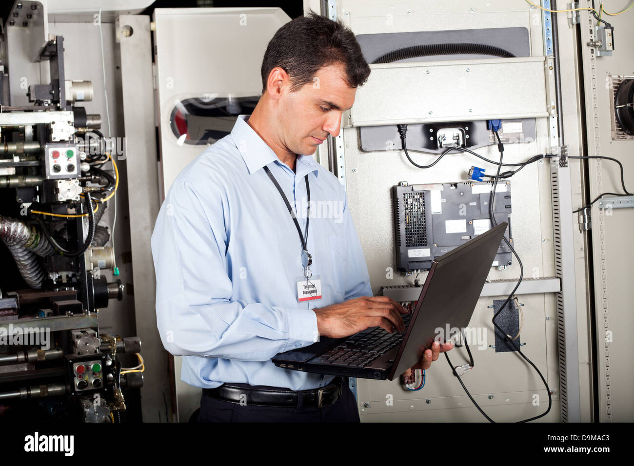 industrial programmer checking computerized machine status with laptop computer Stock Photo