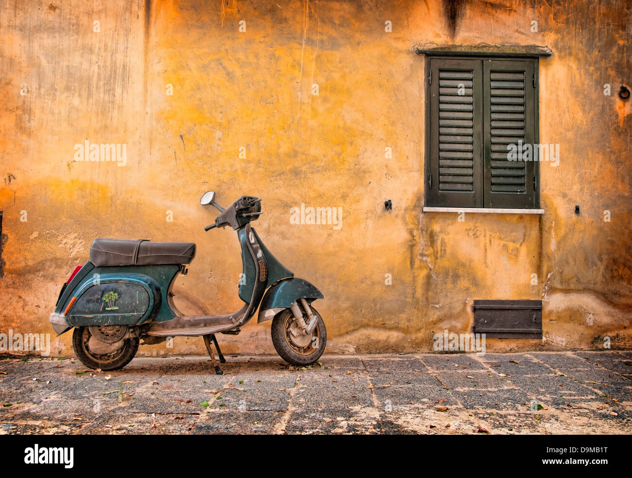Green Vespa Scooter in front of weathered orange wall and green shutters in Castelbuono, Sicily Italy Stock Photo
