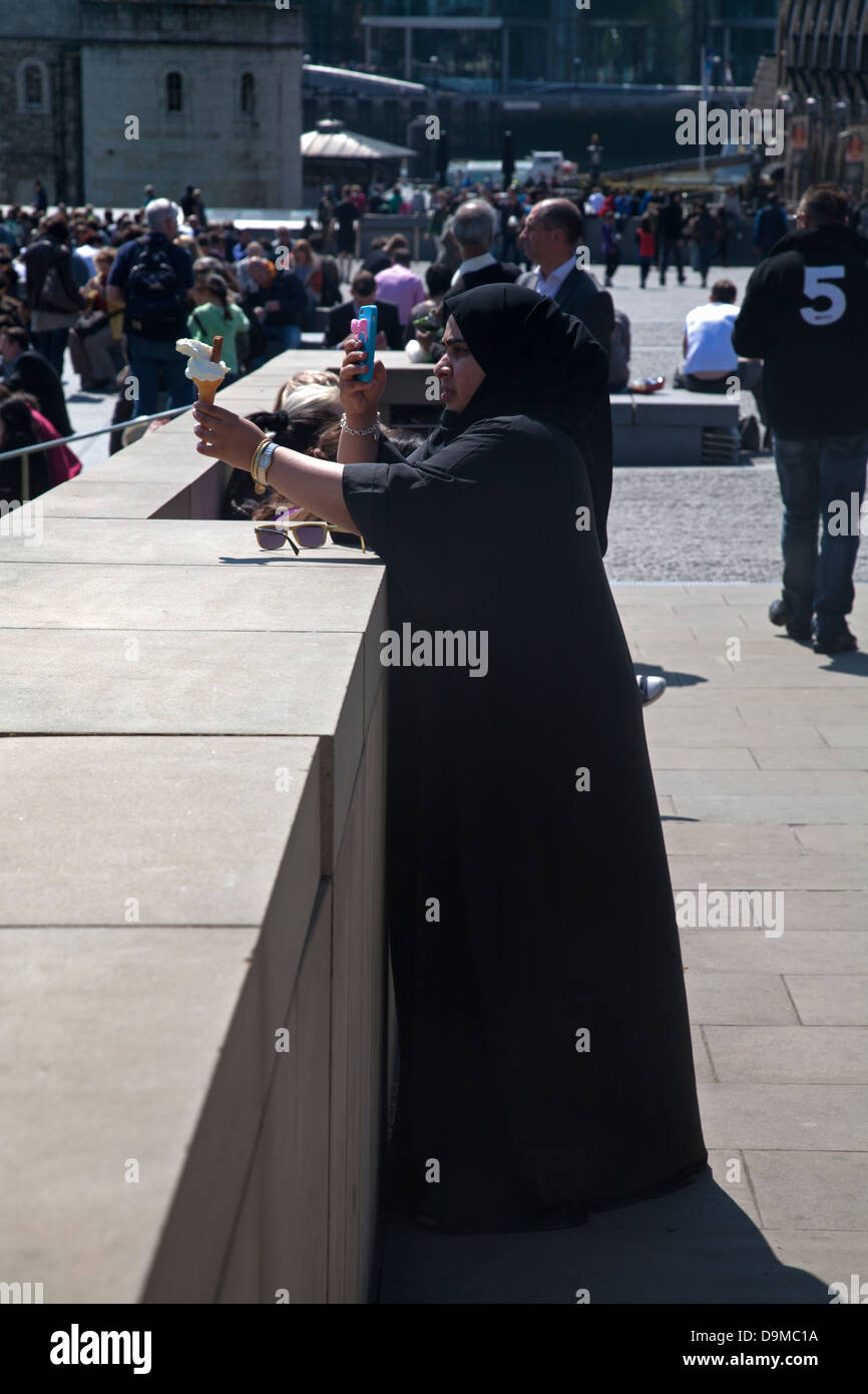 moslem woman photographing ice cream with mobile phone tower hill london england Stock Photo