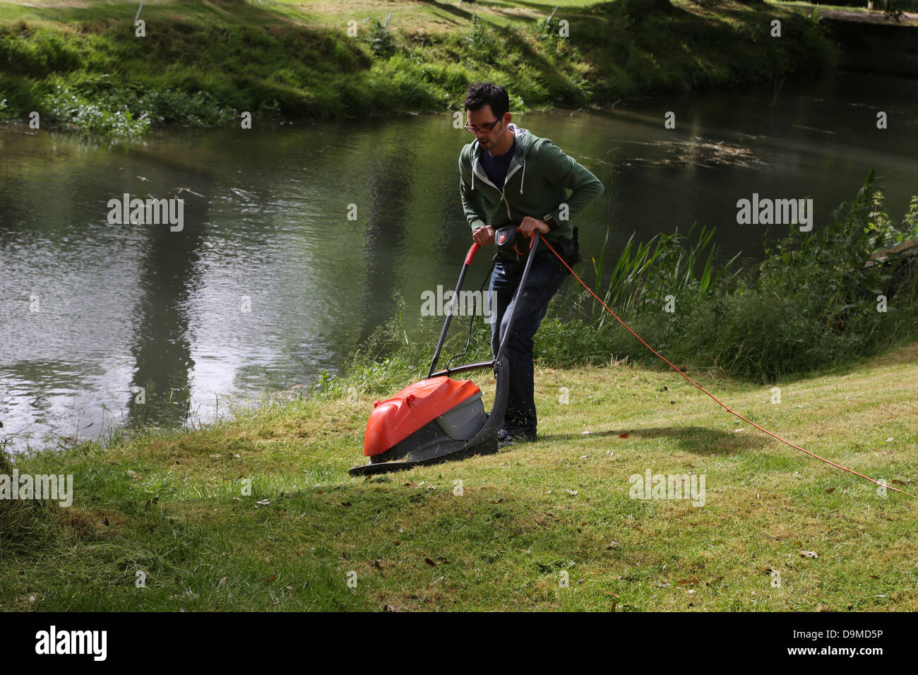 Man Mowing The Lawn With Flymo Lawnmower By River Stour Gillingham Dorset England Stock Photo