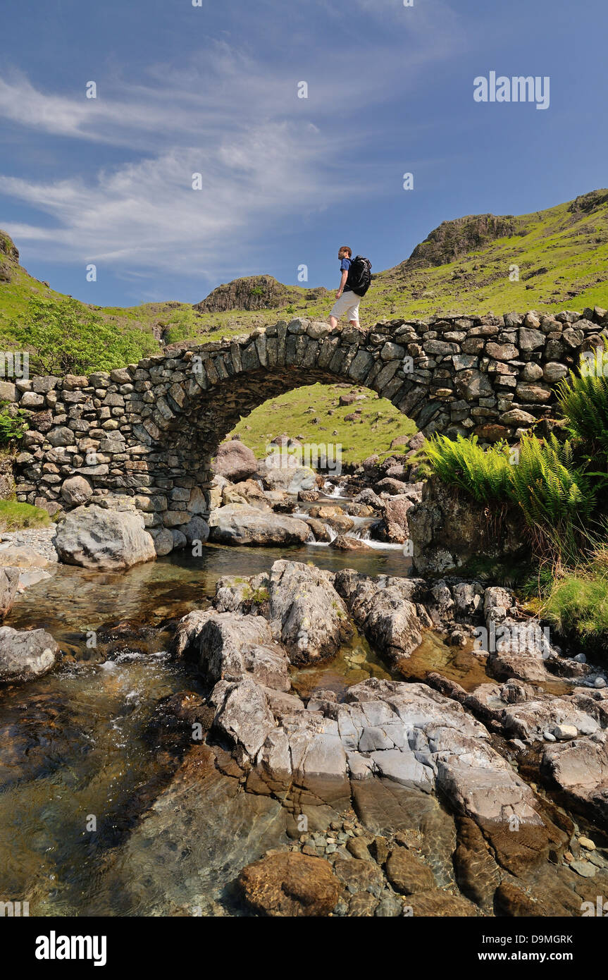 Walker crossing Lingcove Bridge, Upper Eskdale, in summer in the English Lake District Stock Photo